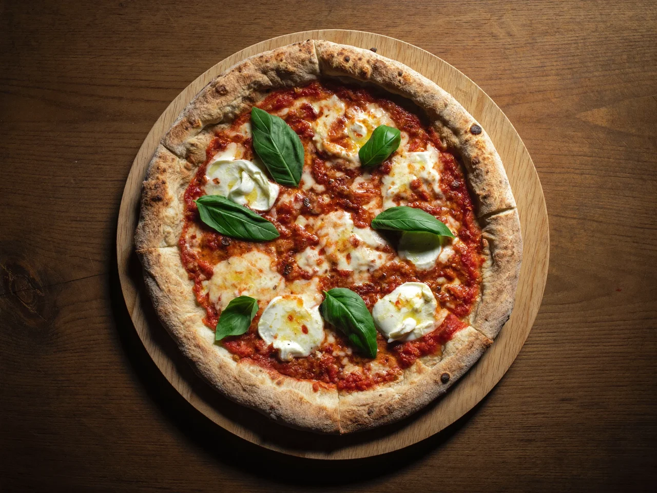 Ganze Pizza Margherita mit Basilikum auf einem schlichten Holzbrett