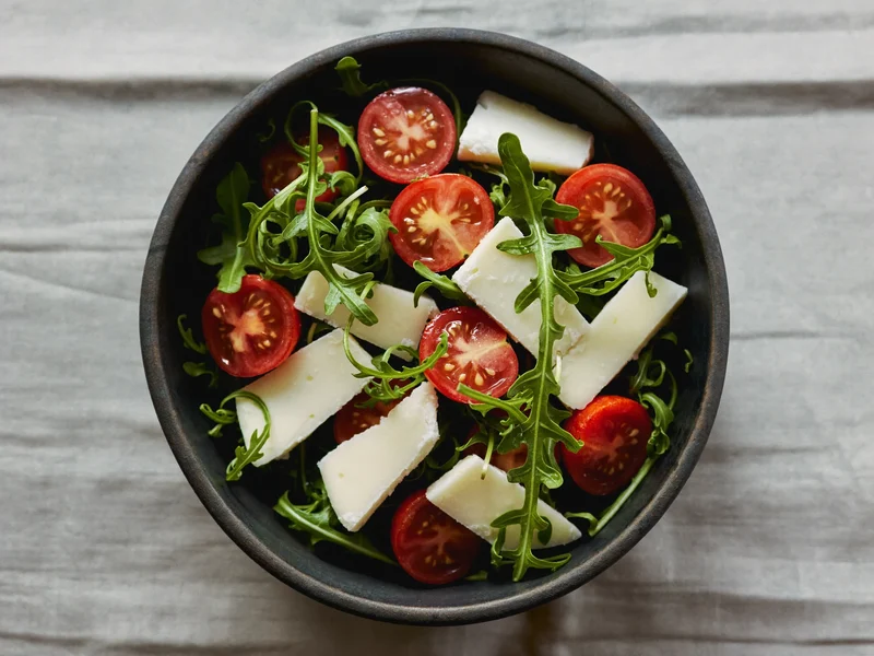 Rucola-Tomaten-Salat mit gehobeltem Käse in einer Steinzeugschale