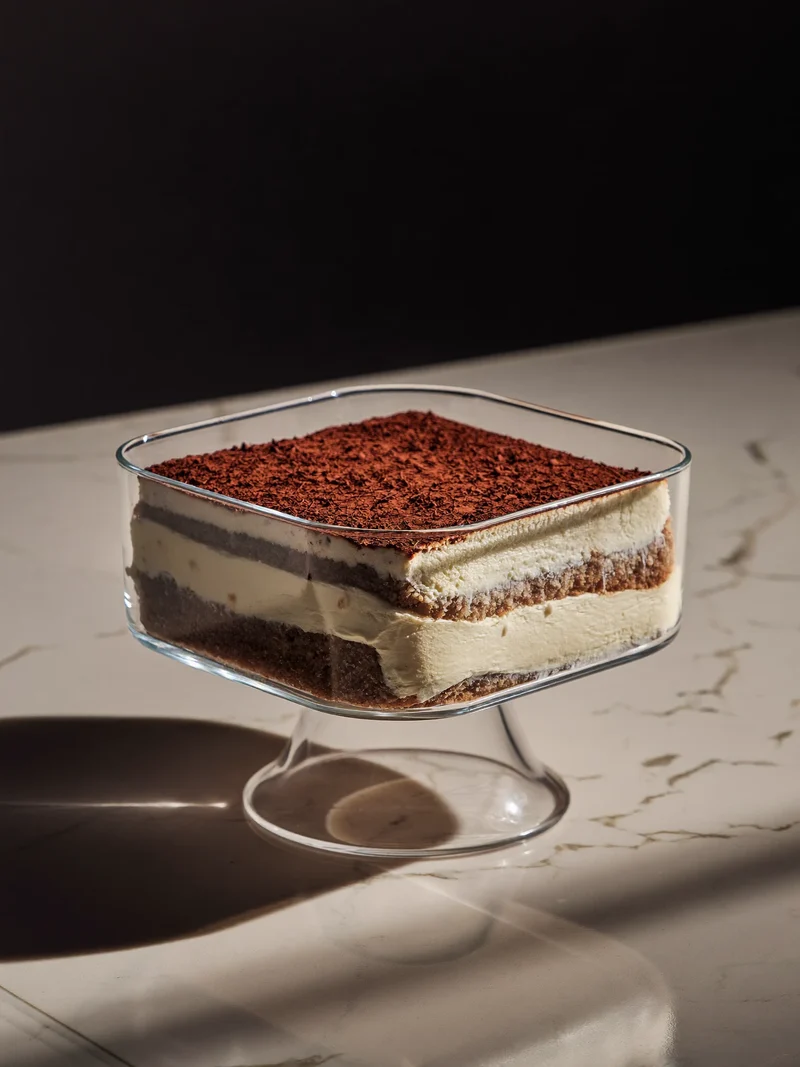 Einzelnes Tiramisu im Glas, mit Kakao bestäubt, auf heller Steinfläche