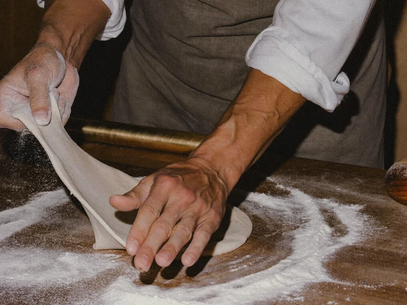 Hände formen Pizzateig auf bemehlter Holzbank